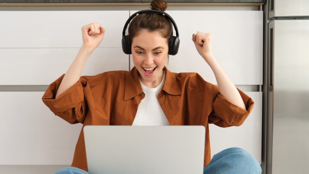 Excited young woman, programmer achieves goal, triumphing, winning on laptop, sitting in headphones, dancing with hands, celebrating victory Excited young woman, programmer achieves goal, triumphing, winning on laptop, sitting in headphones, dancing with hands, celebrating victory